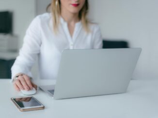 A woman working at a desk using a laptop and smartphone, exemplifying remote work.