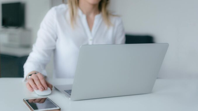 A woman working at a desk using a laptop and smartphone, exemplifying remote work.