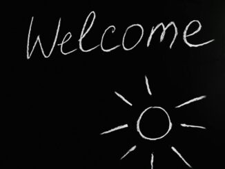 Chalk-drawn 'Welcome' and sun illustration on a black chalkboard background.