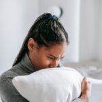 Pensive woman sitting indoors, clutching a pillow with a worried expression.