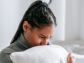 Pensive woman sitting indoors, clutching a pillow with a worried expression.